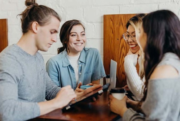 Young adults huddled together in a coffee shop smiling and talking