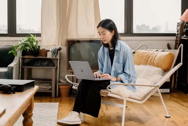 A young asian woman sits in a chair on her laptop